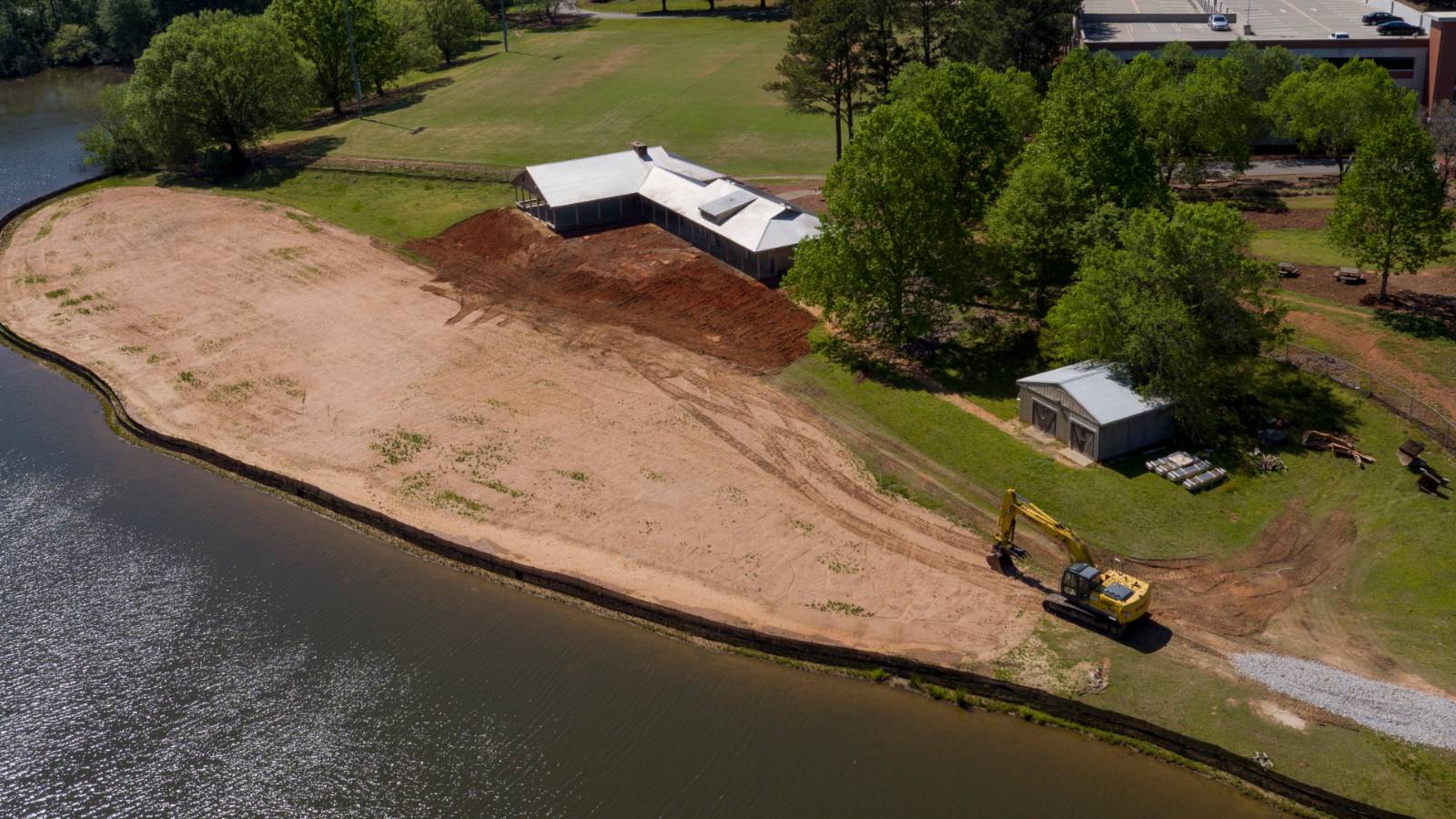 Aerial photo of a lakefront pavilion with construction equipment performing earthwork on the edge of the water
